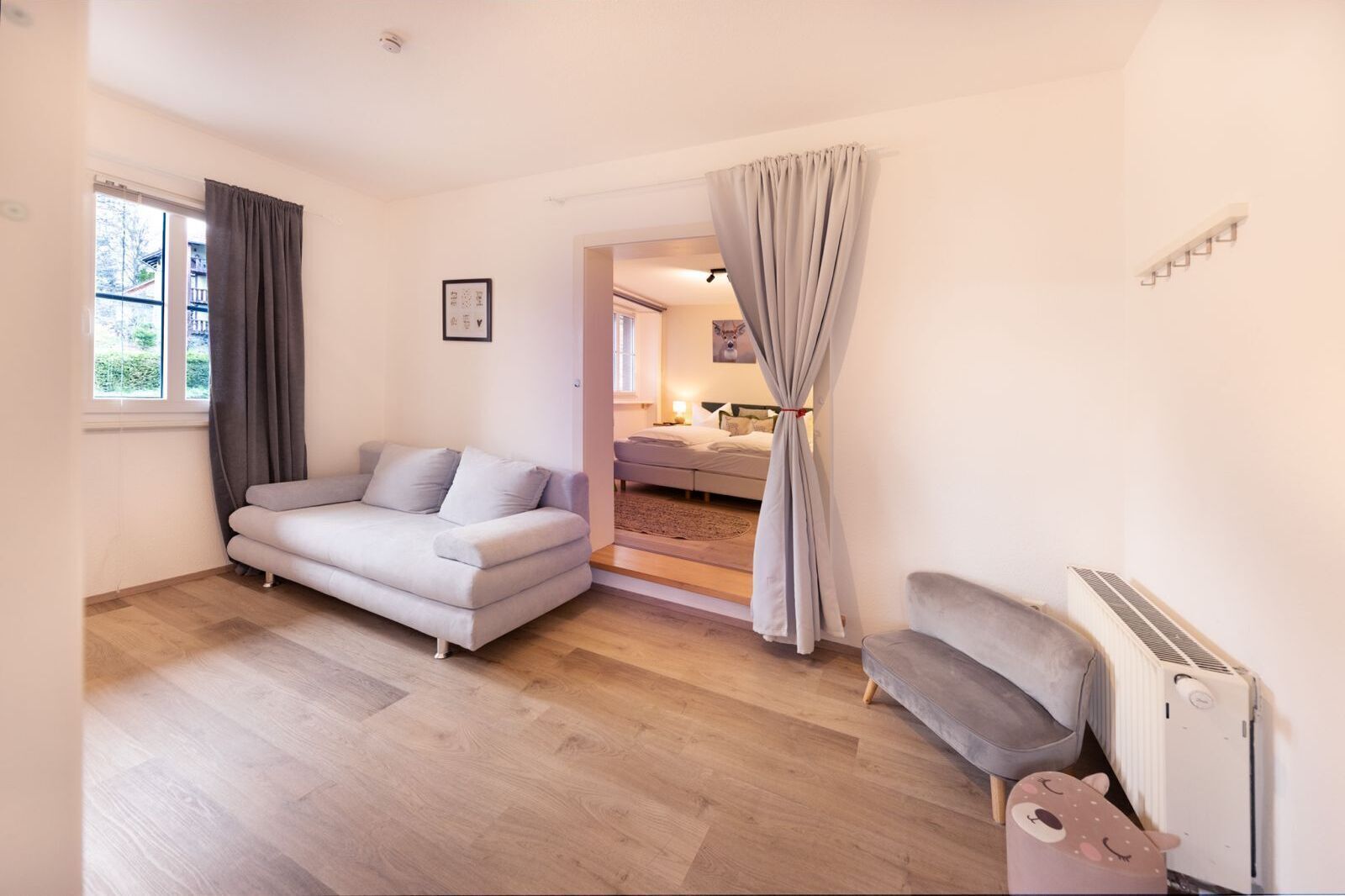 Un salon moderne avec un canapé, un radiateur et une vue sur une chambre à coucher, visible à travers une porte.