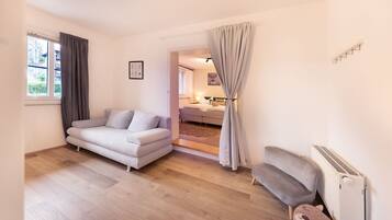 Un salon moderne avec un canapé, un radiateur et une vue sur une chambre à coucher, visible à travers une porte.