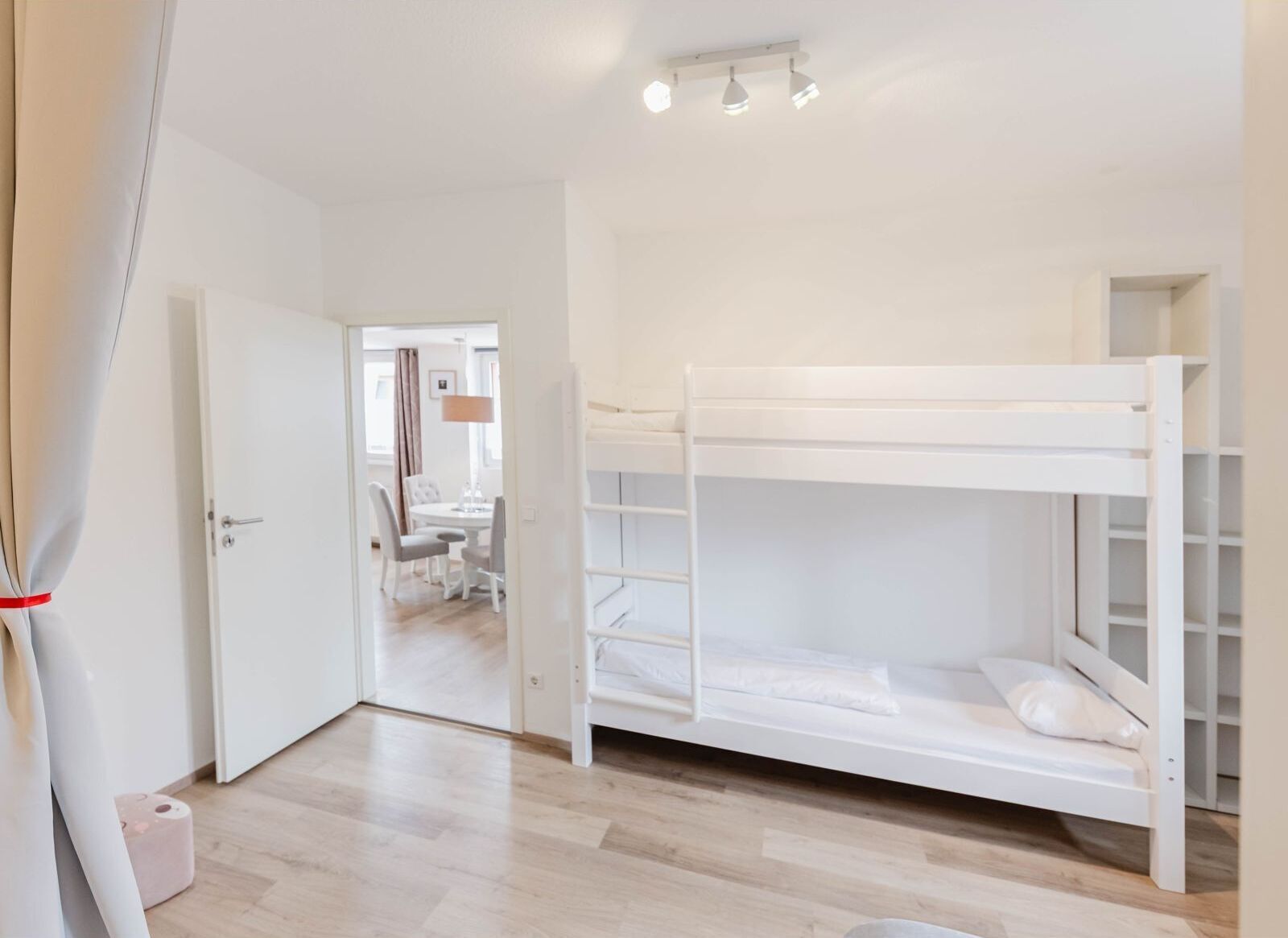 Een kamer met een stapelbed, een deur, een kleine tafel met stoelen en een lamp.