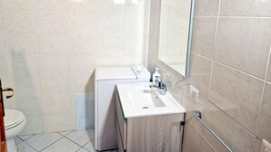 Un baño con lavamanos blanco, espejo y lavadora blanca.