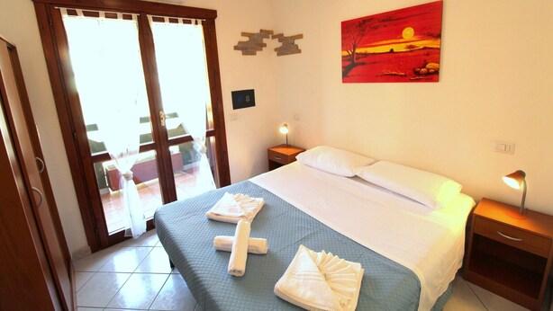 Habitación de hotel con cama, dos mesitas de noche, un cuadro y vistas a través de la puerta de cristal.