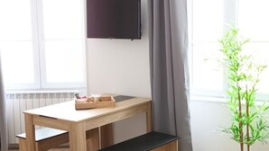 Una habitación con un escritorio de madera, un banco negro, un televisor en la pared y una planta en maceta.