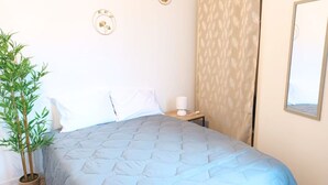 Una cama bien tendida con un edredón azul, una mesita de noche con una lámpara y una planta en maceta.