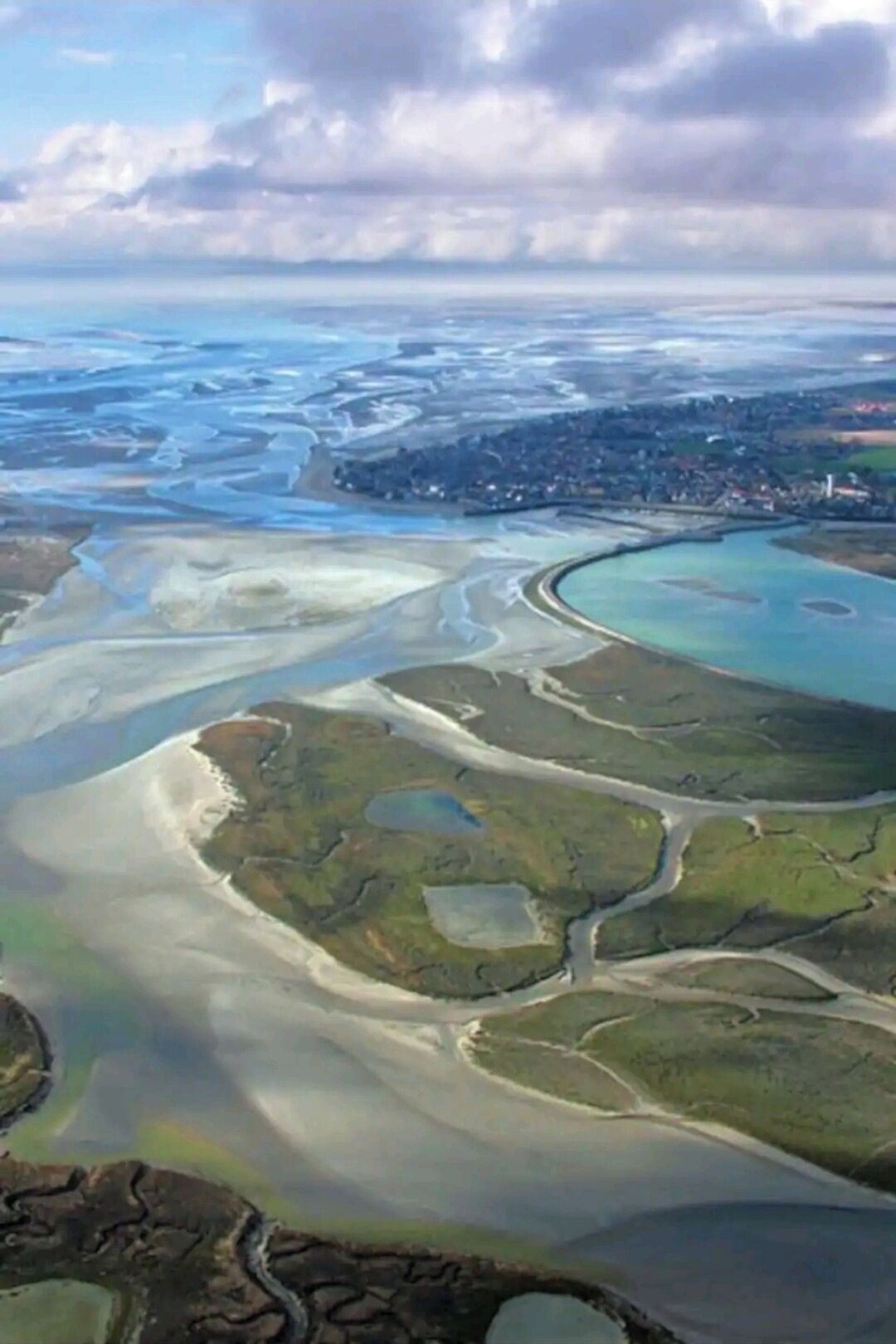 Ett flygbildsbild av ett kustområde med flera vattendrag, inklusive en stor vik och mindre inlopp, omgivet av grönskande land och en stad i fjärran.