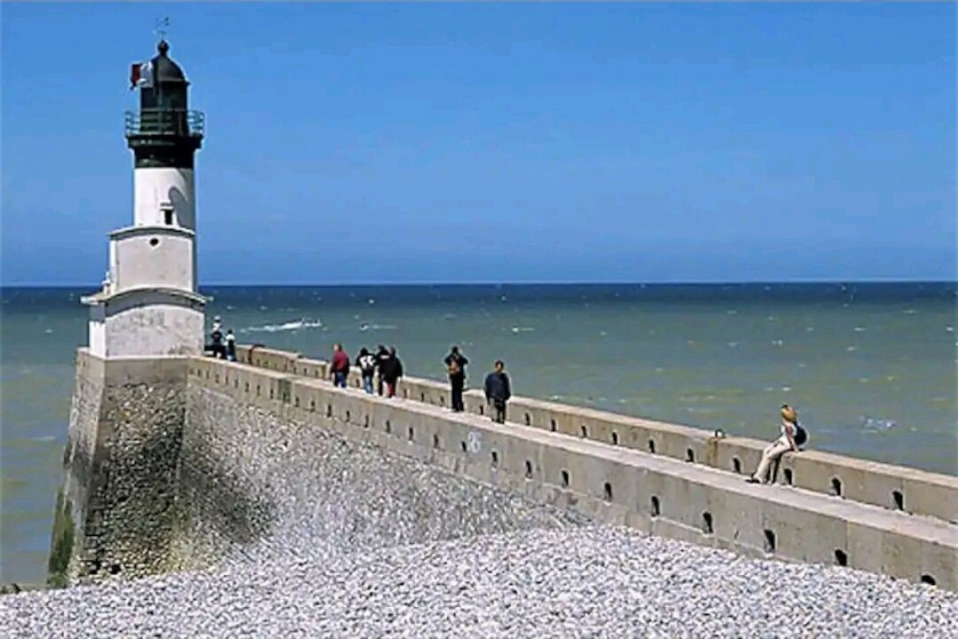 A lighthouse with a concrete walkway leading to it, surrounded by a rocky shoreline.