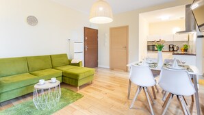 A modern living room with a green sofa, a dining table with white chairs, a small round table with two cups, and a large pendant light. - Vacation apartment by the sea, vacation on the island of Usedom, apartment BALTYCKA 6 (Swinoujscie)