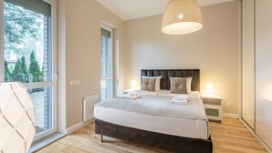 A bedroom with a large bed, a hanging light fixture, a window with blinds, and a view of trees outside. - Vacation apartment by the sea, vacation on the island of Usedom, apartment BALTYCKA 6 (Swinoujscie)