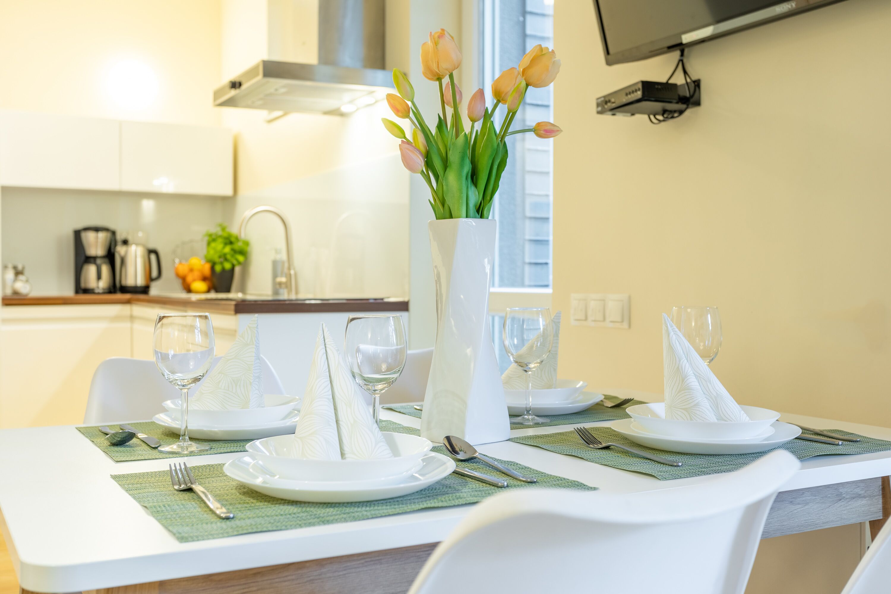 Une table à manger dressée avec de l’argenterie blanche, des couverts et des serviettes, et un vase de fleurs placé sur la table.