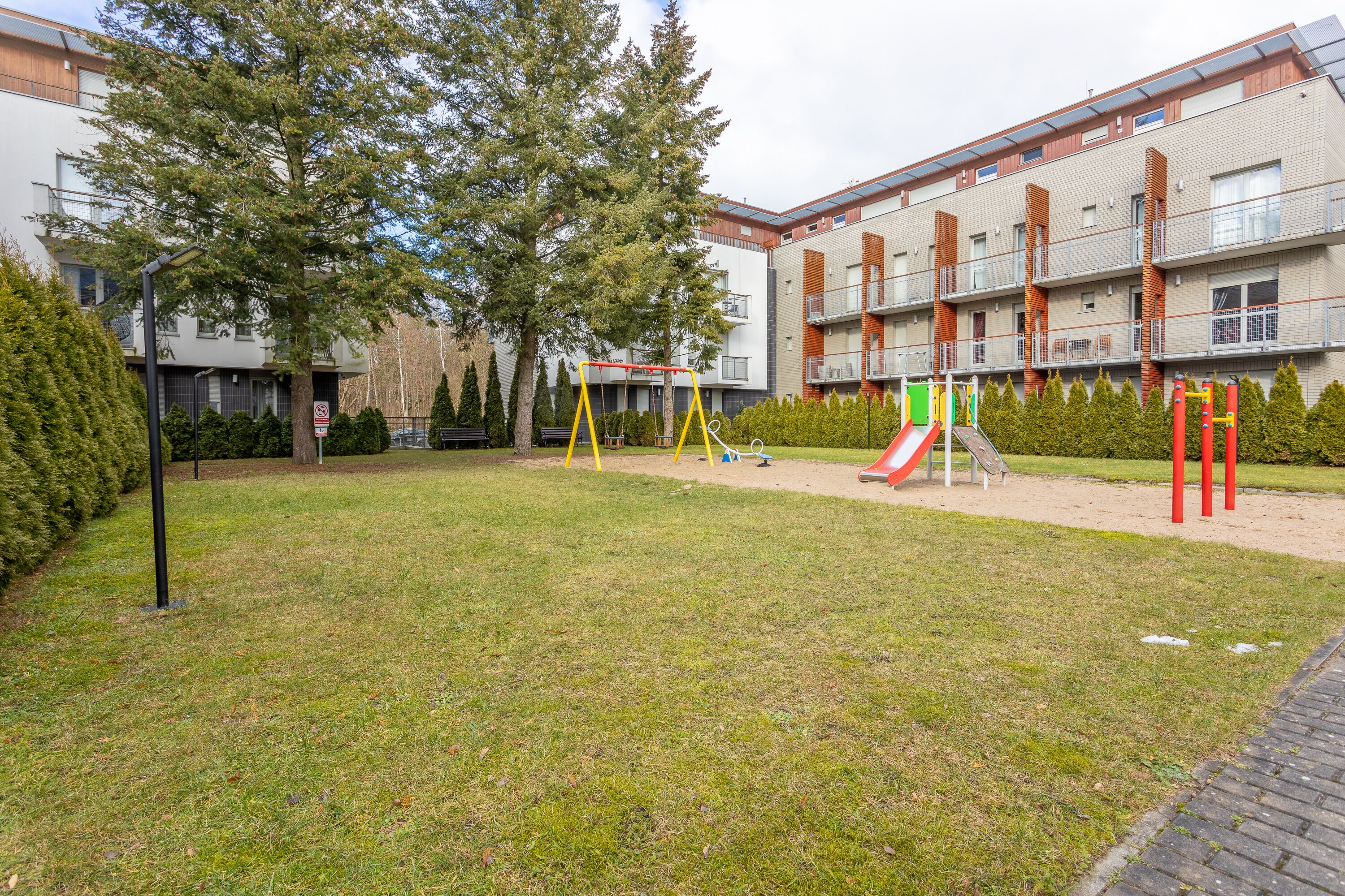 Ein Spielplatz mit Schaukeln und Rutschen, umgeben von Rasen und Bäumen.