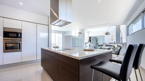 A modern kitchen with a central island, built-in appliances, and a large window providing natural light. - Casa Henna (Faro)