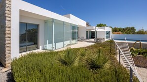 A modern house with large glass windows, a stone exterior, and a patio with outdoor furniture. - Casa Henna (Faro)