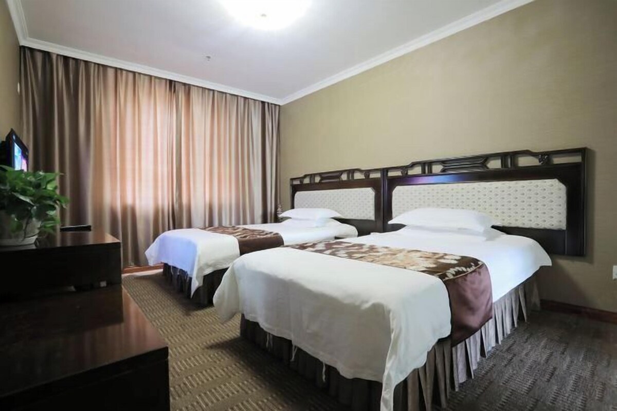 Une chambre d’hôtel avec deux lits, un bureau et une grande fenêtre avec des rideaux.