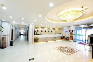 A hotel lobby with a reception desk, a chandelier, a patterned floor design, and a long corridor. - Xiyu Yongsheng Hotel (Fuyun)