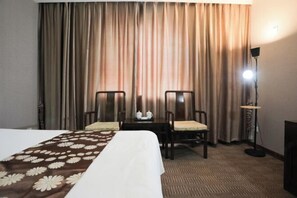Une chambre d’hôtel avec un lit, deux chaises, une table avec une théière et des tasses, une lampe et des rideaux.