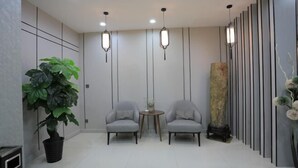 Eine moderne Lobby mit zwei grauen Sesseln, einem kleinen runden Tisch, einer großen Kühlpflanze und einer hohen Säule mit vertikalen Linien.