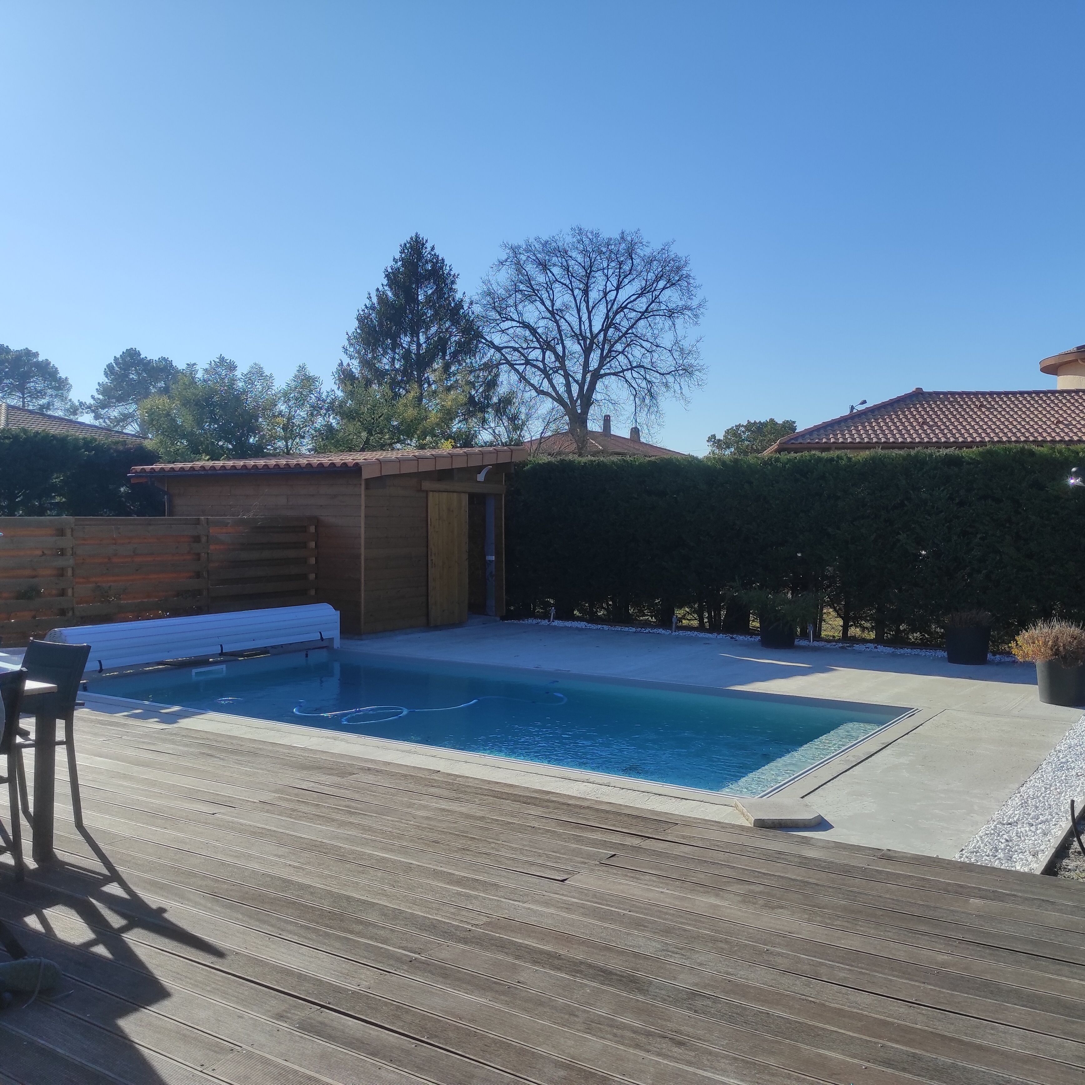 Un pontile in legno con piscina, un capanno di legno e un siepe.
