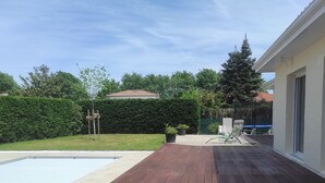 Een houten terras met een zwembad, plantenpotten en een haag op de achtergrond.