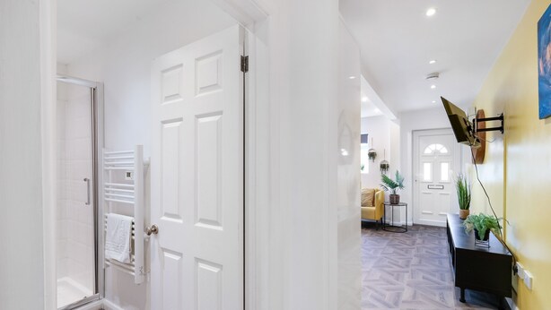 A hallway with a glass door leading to a shower area, a white door, and a wall-mounted TV.