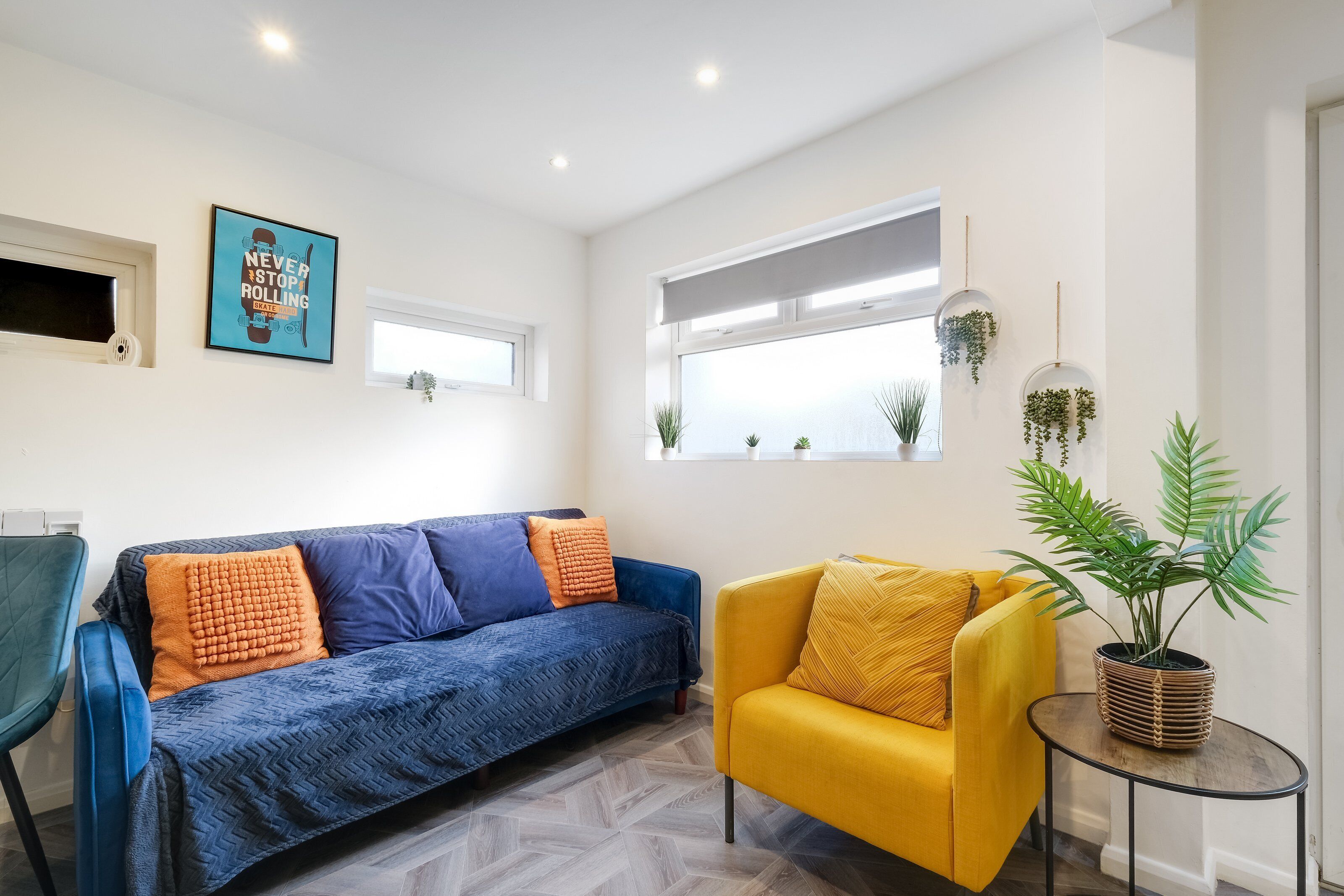 A modern living room with a blue sofa, a yellow armchair, and a small table with a plant.