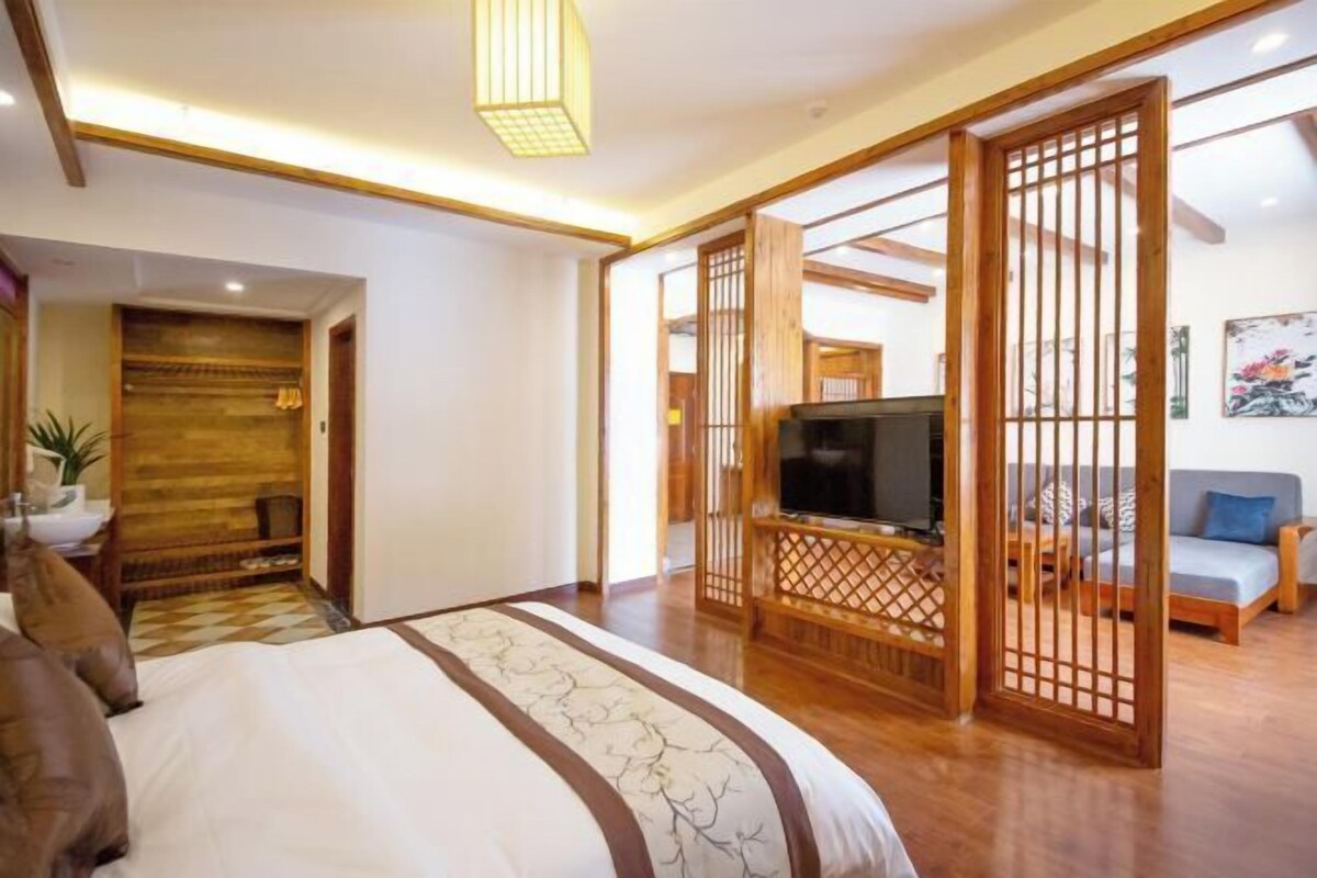 A hotel room with a bed, a TV, a sofa, and a wooden partition.