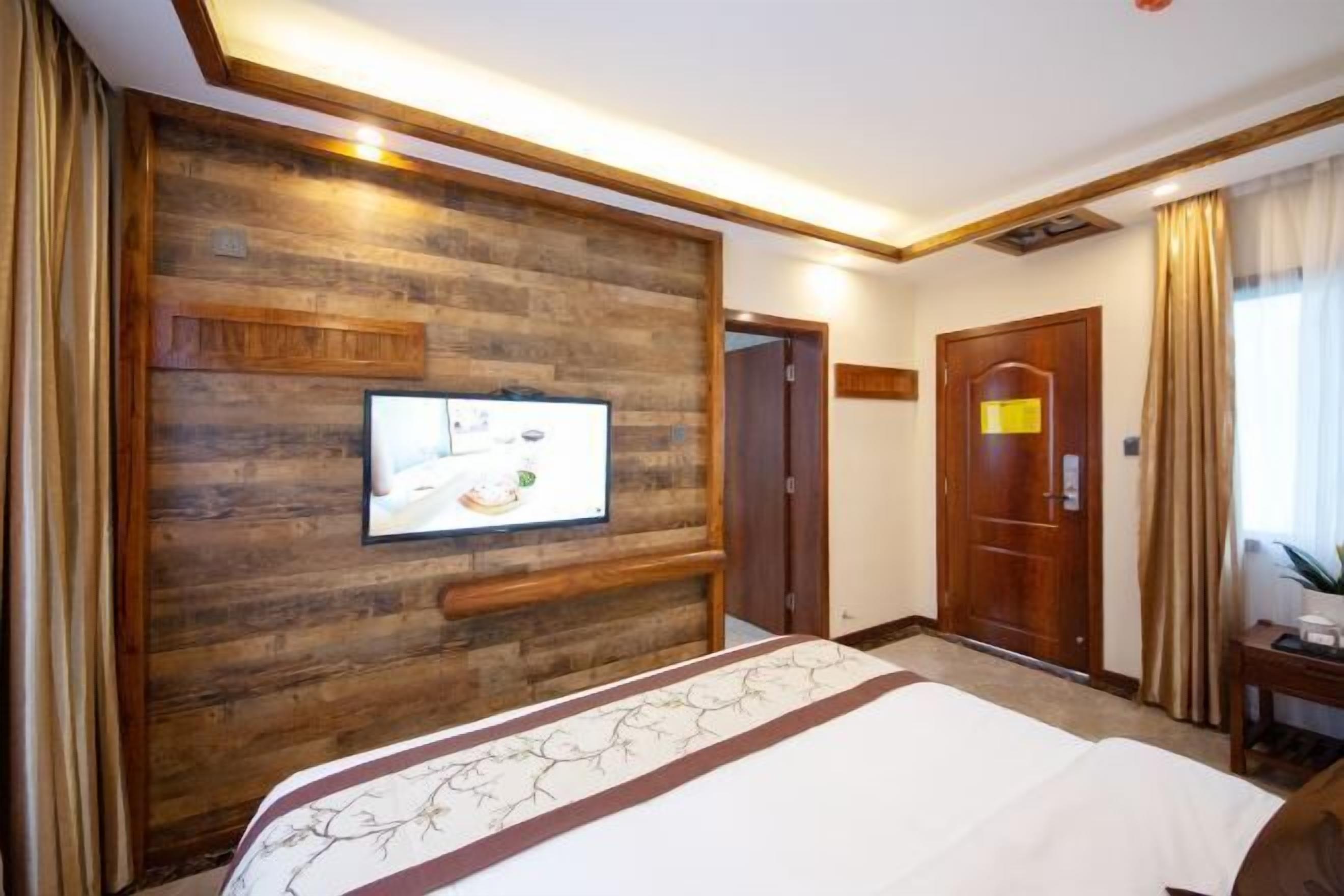 A hotel room with a wooden accent wall, a flat-screen TV, a bed with a floral bedspread, a desk with a chair, and a door leading to another room.