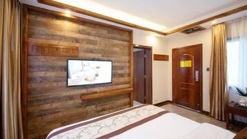 A hotel room with a wooden accent wall, a flat-screen TV, a bed with a floral bedspread, a desk with a chair, and a door leading to another room.