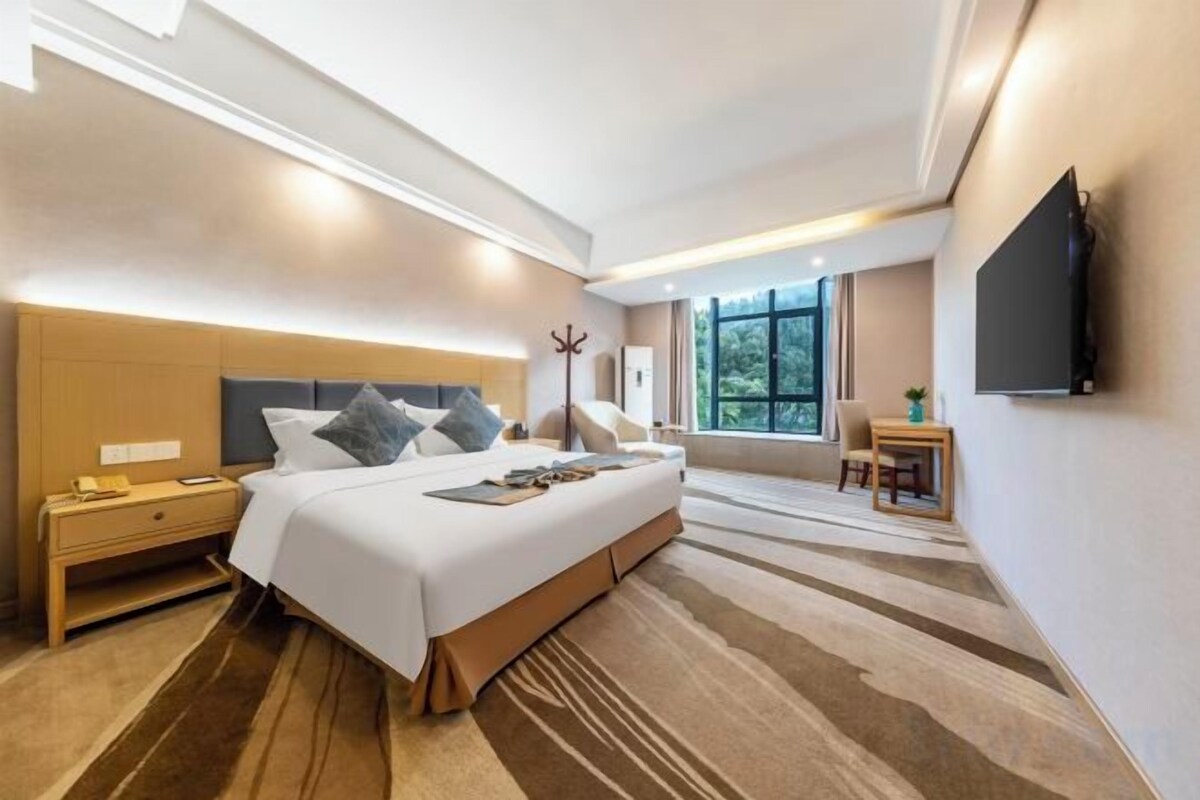 Une chambre d’hôtel moderne dotée d’un grand lit, de tables de chevet, d’un téléviseur à écran plat et d’une fenêtre offrant une vue agréable.