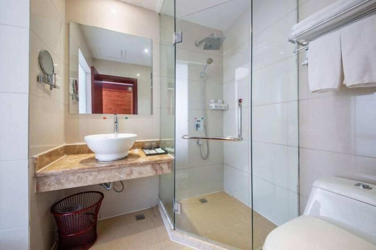 Uma casa de banho moderna com chuveiro envolto em vidro, lavatório branco e sanita.