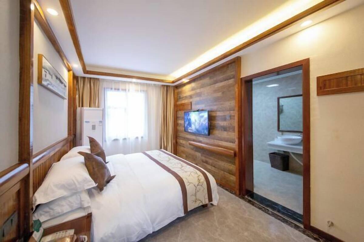 Quarto de hotel com cama, televisão, banheiro com pia e uma porta deslizante.