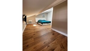 Un dormitorio con suelo de madera, una cama con colcha verde, cabecero blanco y una ventana pequeña.