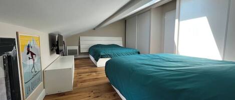 A bedroom with two beds, a desk, and a window.