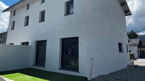 Un edificio moderno de dos pisos con techo plano, ventanas grandes y una pequeña zona de césped verde al frente.