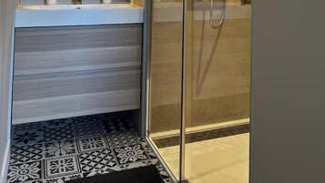 Une salle de bain moderne avec une douche à l’italienne en verre, un grand miroir et un sol carrelé.