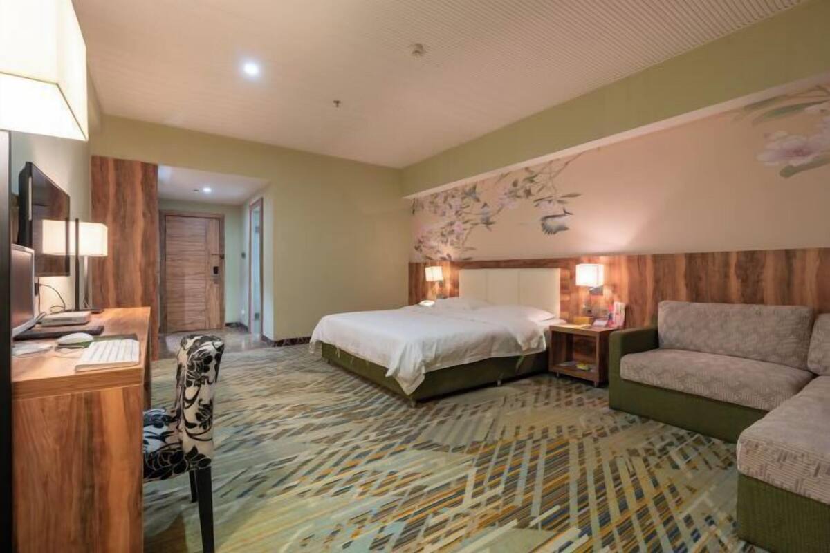 A hotel room with a bed, a desk with a computer, a chair, and a sofa.