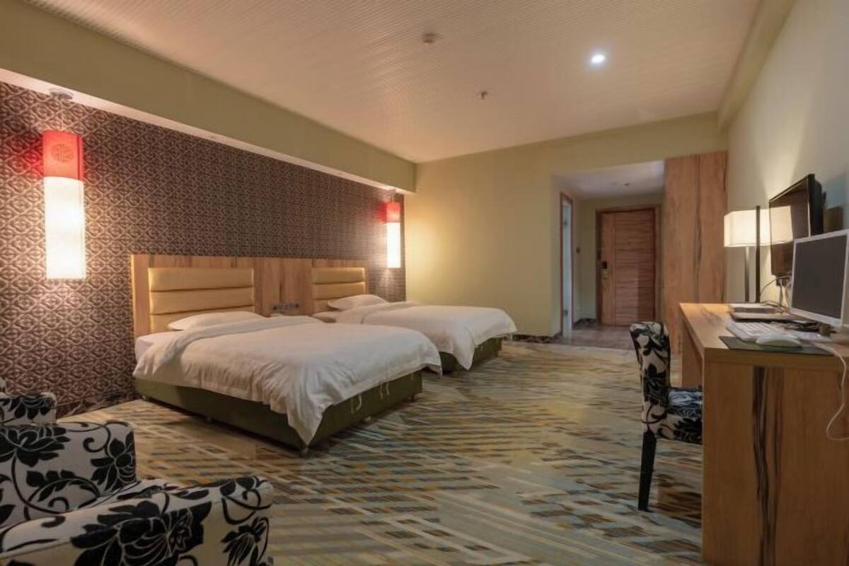 A hotel room with two beds, a desk with a computer, and a patterned carpet.