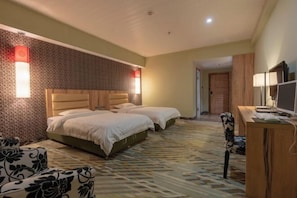 A hotel room with two beds, a desk with a computer, and a patterned carpet.