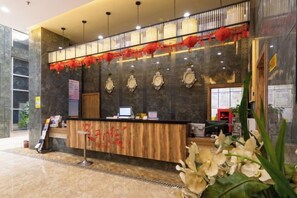 A hotel reception area with a wooden reception desk, a computer, and a wall with decorative elements.