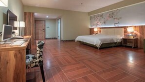 Ein Hotelzimmer mit Schreibtisch aus Holz, Computer, Stuhl, Bett und einer Wand mit floralem Wandbild.
