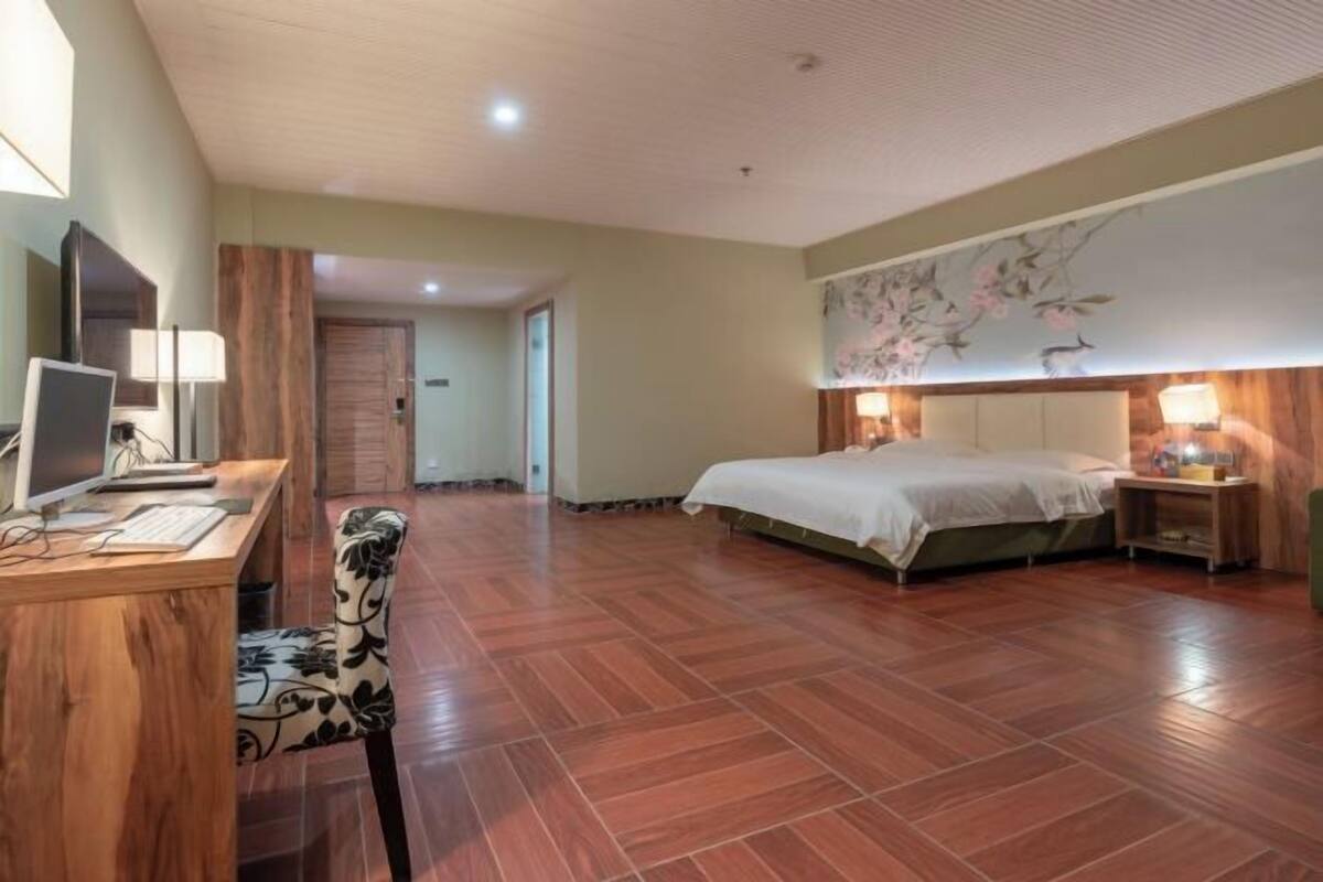 A hotel room with a wooden desk, computer, chair, bed, and a wall with a floral mural.