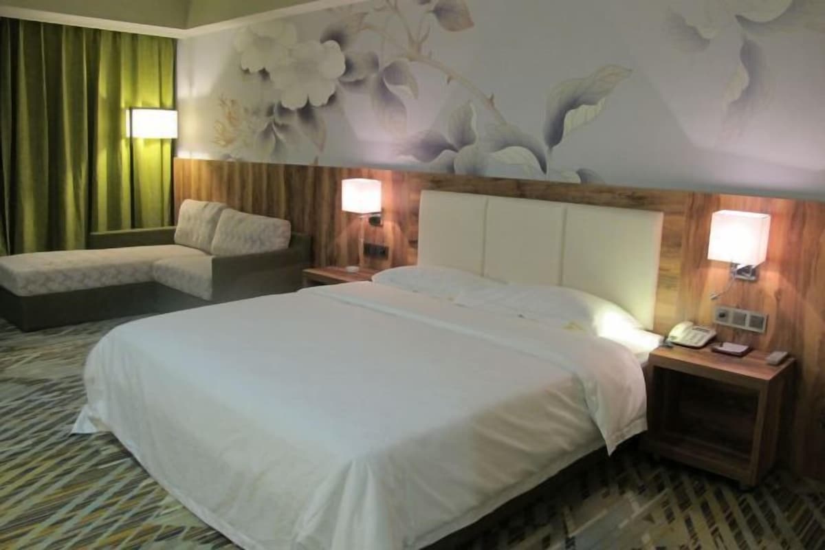 A hotel room with a large bed, a sofa, two bedside tables with lamps, and a floral wall mural.