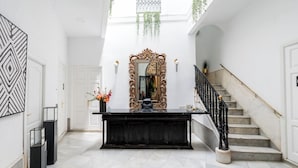 A grand foyer with a marble staircase, a large ornate mirror, and a black console table. - Hostal Roomsole (Seville)