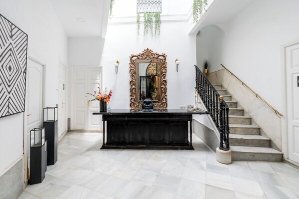 A grand foyer with a marble staircase, a large ornate mirror, and a black console table. - Hostal Roomsole (Seville)