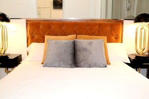Una cama bien tendida con cabecera acolchada, dos lámparas de noche y dos almohadas.