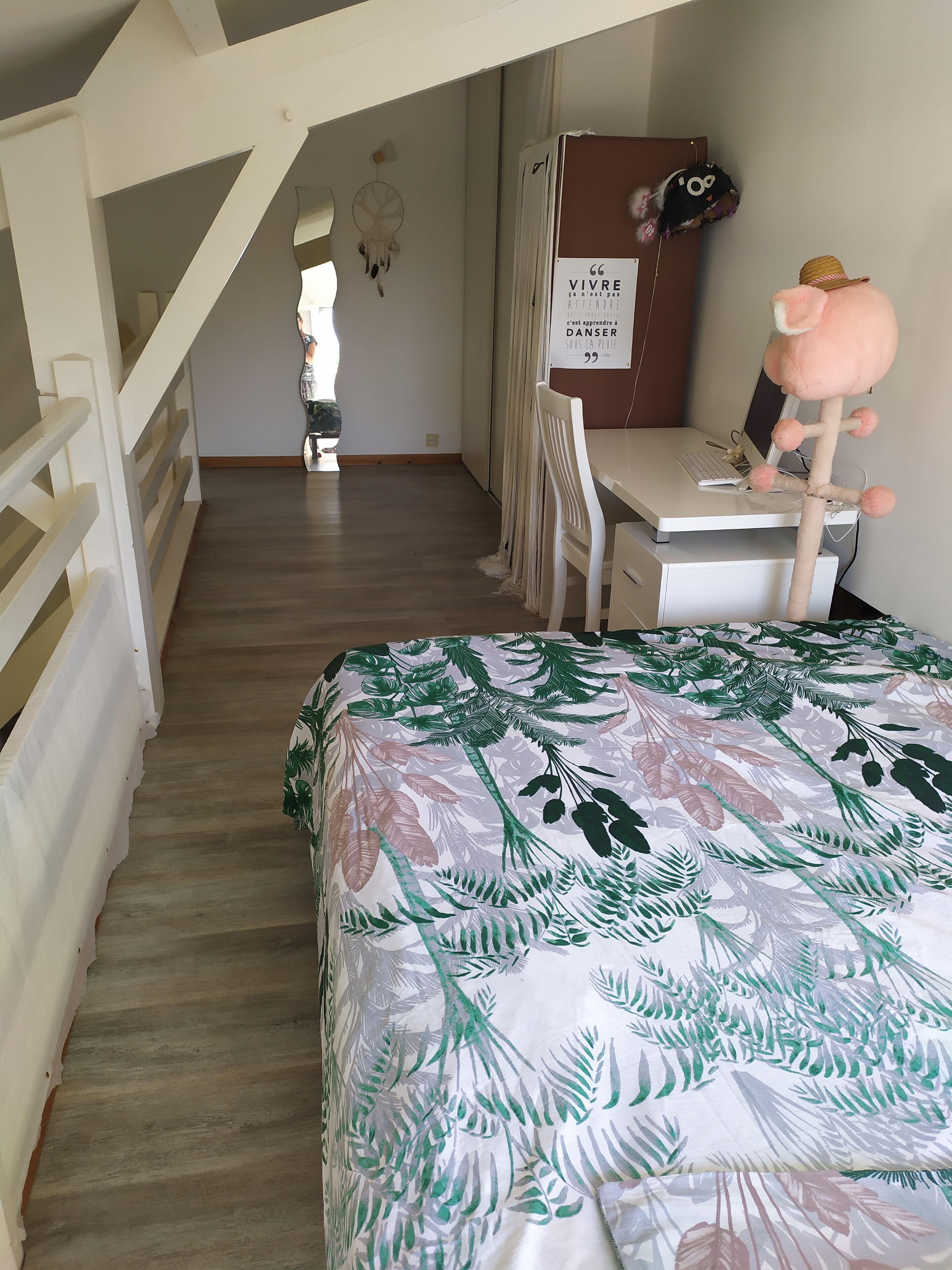 A bedroom with a bed, a desk, and a chair. There is a staircase leading to another room.