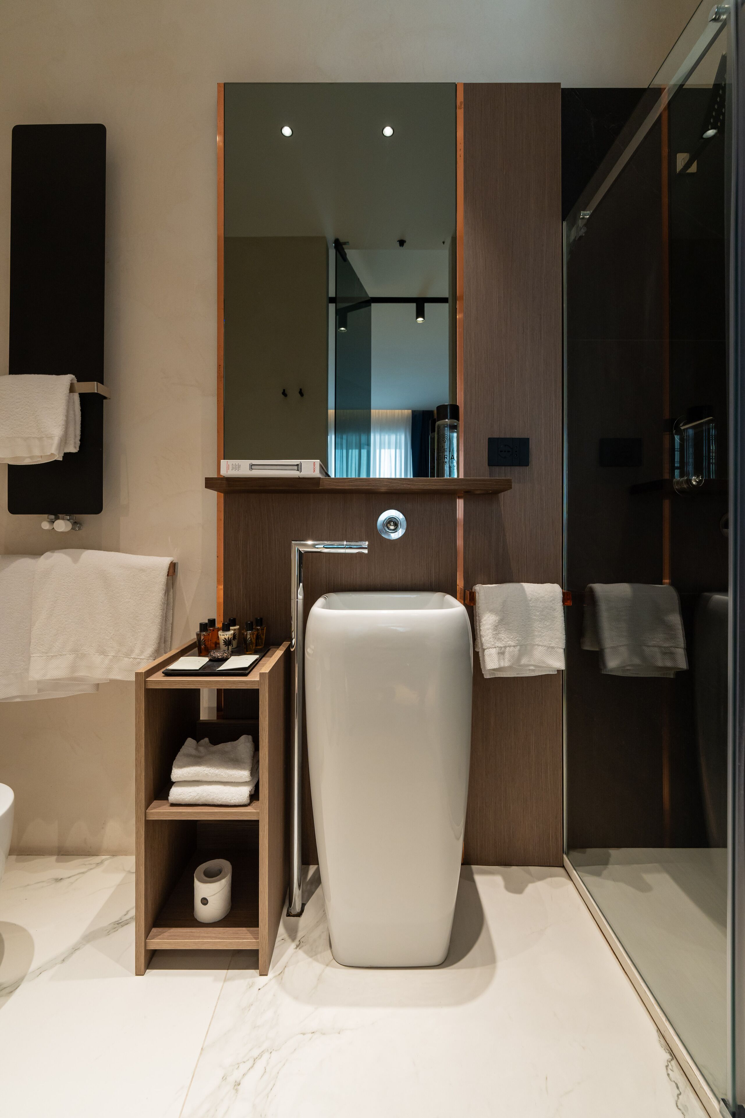 Un bagno moderno con un grande specchio, un lavandino bianco, box doccia in vetro e uno scaffale in legno con asciugamani.