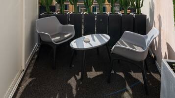 A rooftop terrace with two white chairs and a small table, surrounded by potted cacti.