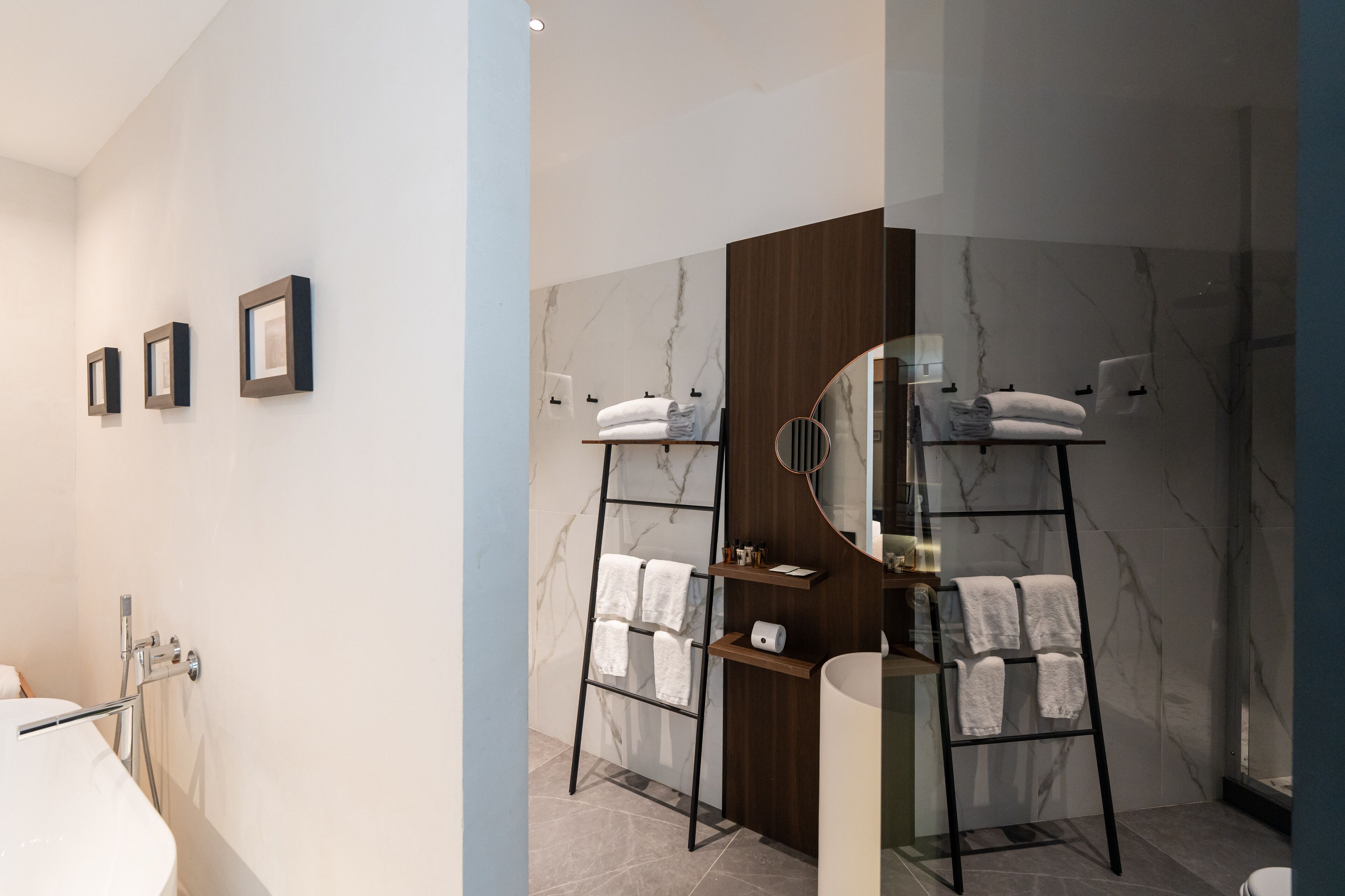 A modern bathroom with a marble wall, a wooden vanity, a freestanding bathtub, and a towel rack.