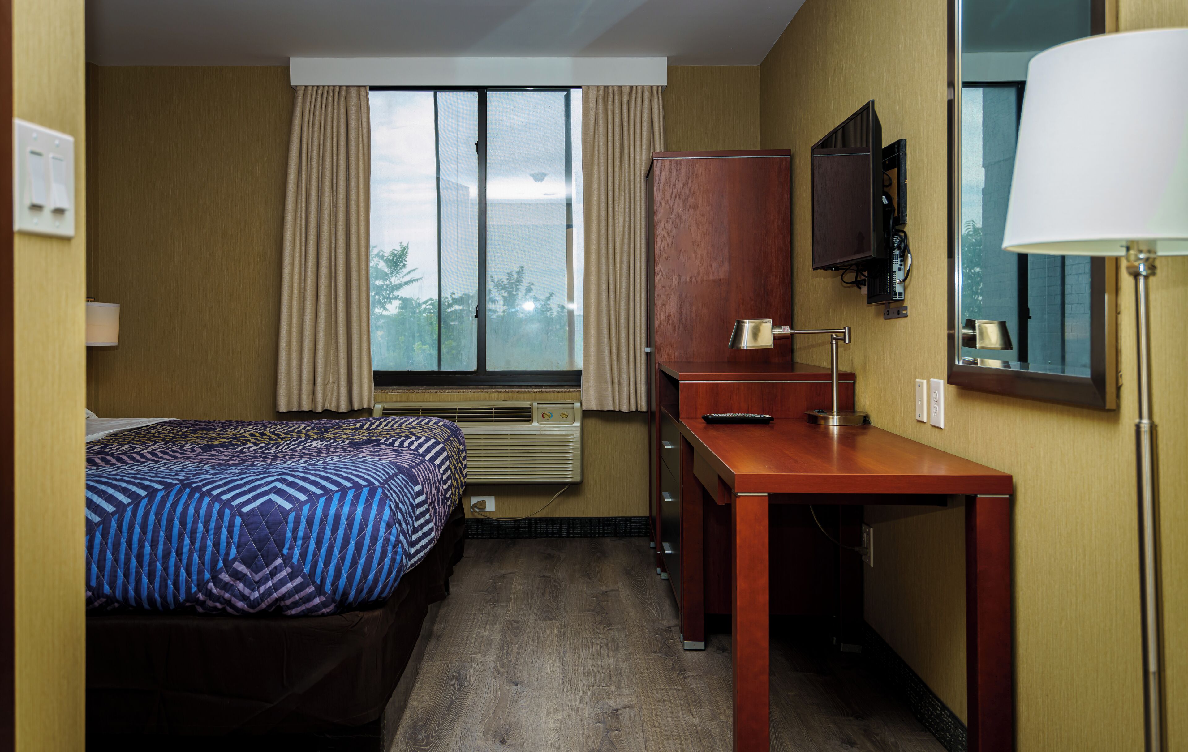 A hotel room with a bed, a desk, a television, and a window with curtains.
