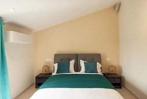 A bedroom with a bed, two nightstands, a wall-mounted air conditioner, and a curtain.
