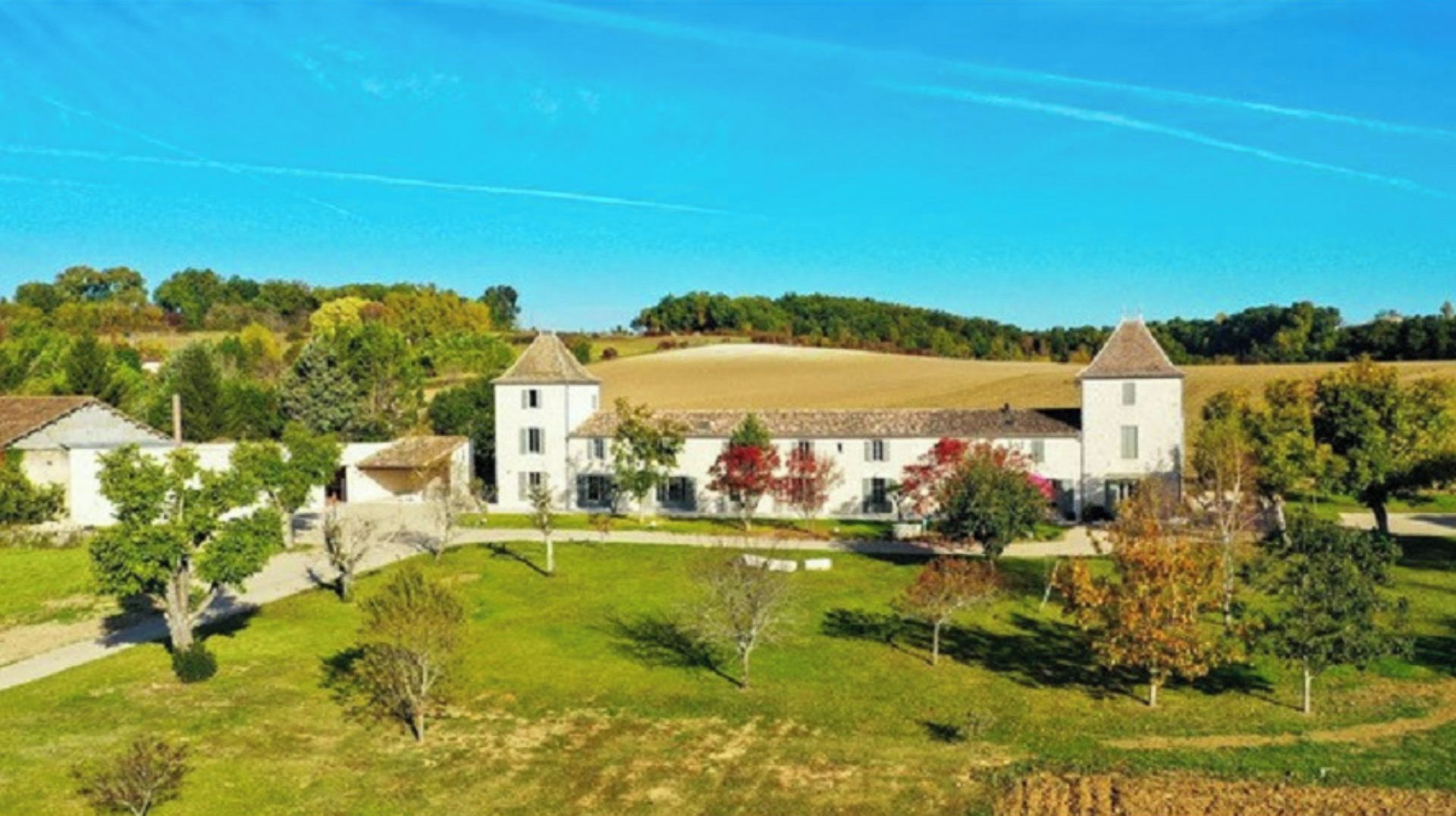 A large estate with multiple buildings, including a central white structure with a tower, surrounded by open fields and trees.